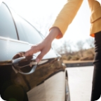 A hand grabs the door handle of a car.